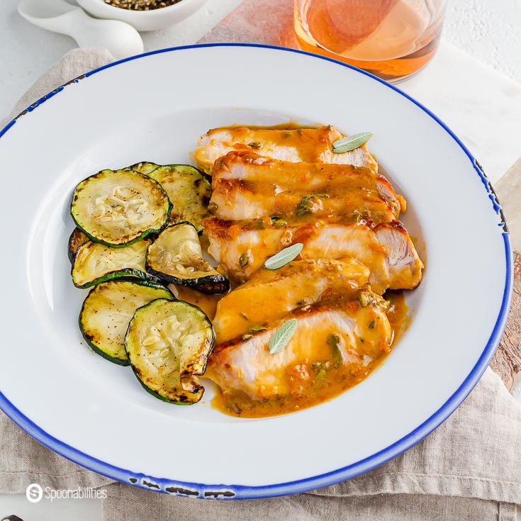 A close up photo of a white plate with pan-seared pork chops with the creamy apricot Dijon mustard sauce. The side dish on the pork is pan-fried zucchini. Recipe at Spoonabilities.com