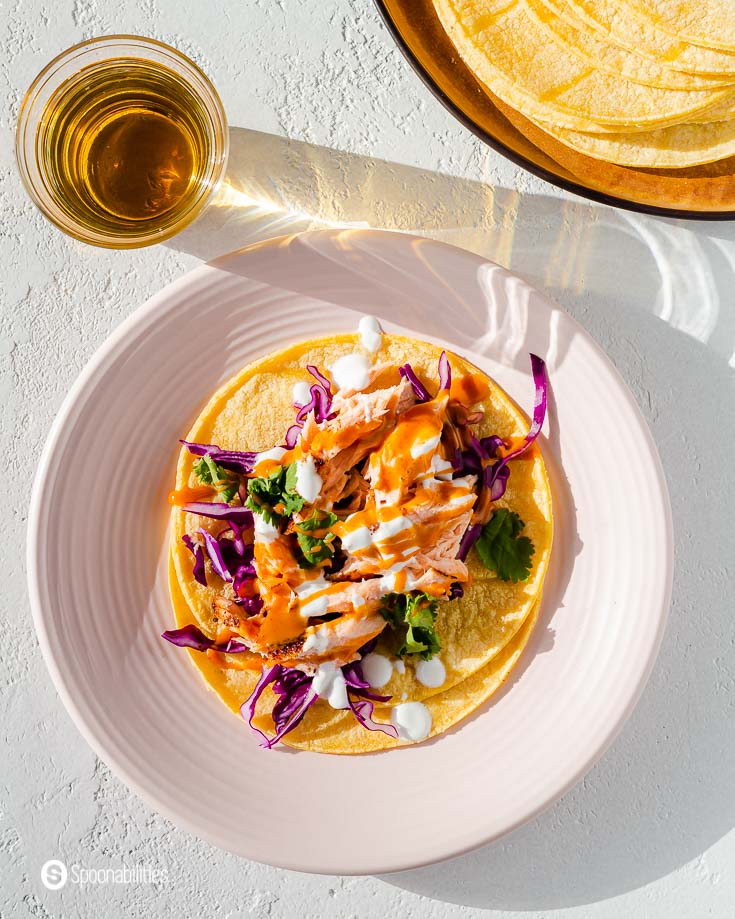 One pink round plate with fish tacos made out of a salmon-filled cooked in the air fryer. Garnished with red cabbage, spicy chipotle sauce, cilantro, and Mexican Crema. recipe at Spoonabilities.com