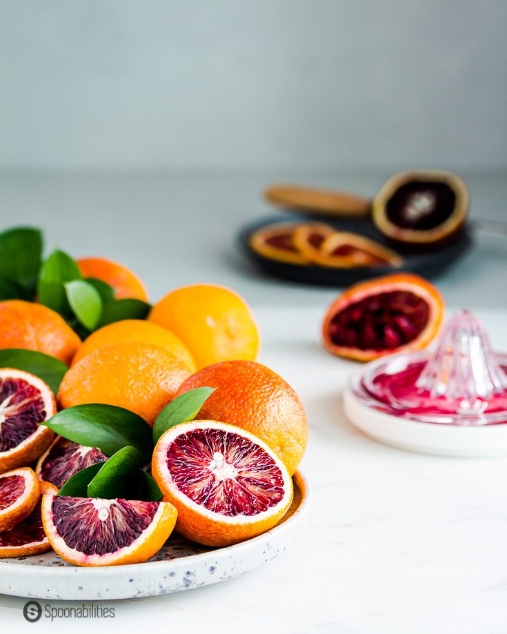 A bunch of fresh blood orange on a grey plate with Some oranges showing the fruits red hue color. Recipe at Spoonabilities.com