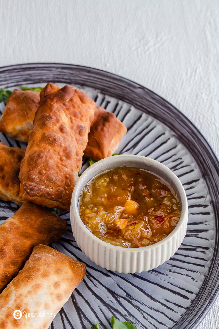 A plate with a few veggie egg rolls and a small bowl with roasted pineapple habanero dipping sauce. This sauce is perfect for spring rolls, wings, chicken, and more. Find this product from Terrapin Ridge at Spoonabilities.com