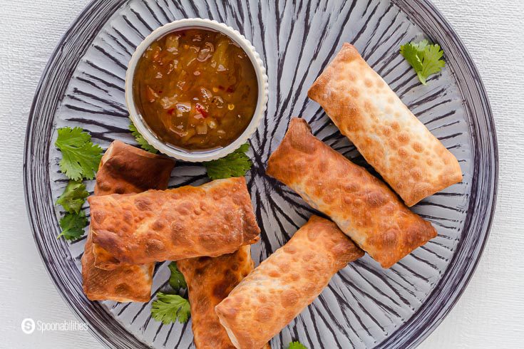 A Close up photo of a grey plate with six egg rolls cooked in the air fryer and a small bowl with Roasted pineapple habanero sauce. Recipe at Spoonabilities.com