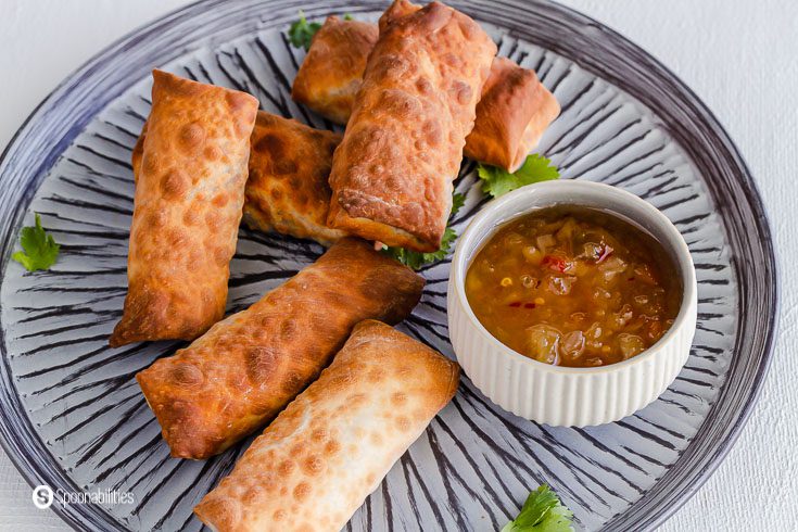 close up photo of the crispy golden egg rolls filled with sautee vegetables. On the plate a small bowl with roasted pineapple habanero dipping sauce. Recipe at spoonabilities.com