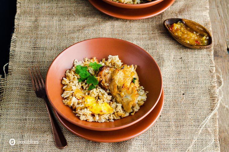 A terracotta style plate with chicken and rice. Garnished with a piece of roasted pineapple and fresh cilantro. Recipe at Spoonabilities.com
