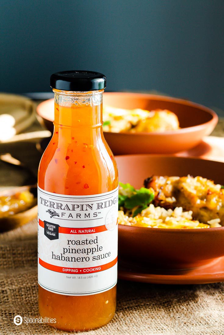 A glass bottle with roasted pineapple habanero sauce by Terrapin Ridge, The bottle is in front of a grown plate with chicken and rice. Recipe at Spoonabilities.com