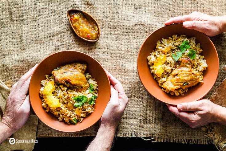 Two people hands holding two terracotta color bowls with chicken and rice casserole. Recipe at Spoonabilities.com