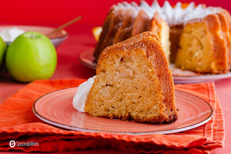 A piece of apple cake made out of olive oil and Granny Smith apples. The slice of cake is on a small plate on top of an orange napkin. Recipe at Spoonabilities.com