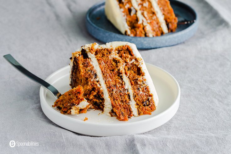 White plate with a piece of carrot cake and in the background another plate with cake. recipe at Spoonabilities.com