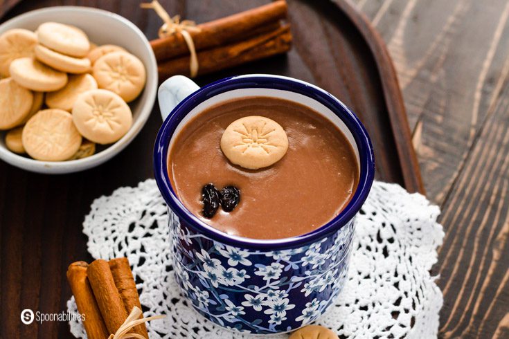 A close-up of a blue printed cup with Habichuelas con dulce garnished with milk cookies and raisins. Learn the ingredients at Spoonabilities.com