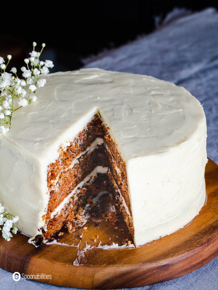 A photo with a whole cake showing some of the carrot cake insides and outside with the cream cheese frosting. Recipe at Spoonabilities.com