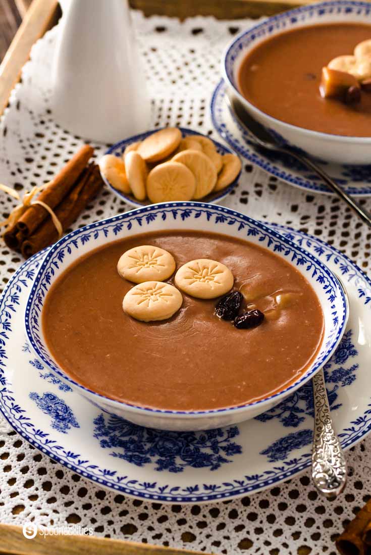 An antique-looking bowl with blue imprints with a traditional Dominican dessert in the bowl. This dessert is made with red kidney beans, coconut milk, evaporated milk, cinnamon sticks, whole cloves, sugar, and raisins. Learn more about this Easter dessert at @spoonabilities.com