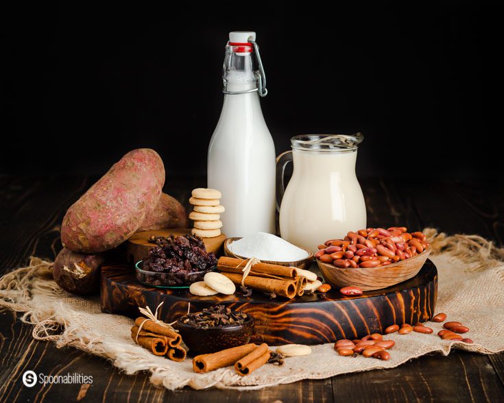 The photo shows all the ingredients used in this Dominican Easter recipe, and some of the ingredients are red kidney beans, coconut milk, evaporated milk, sugar, cinnamon sticks, white sweet potatoes, milk cookies, and raisins. Learn more about this Dominican recipe at @Spoonabilities.com