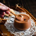 En la foto hay una taza de cristal con el dulce Dominicano que tradicionalmente se sirve durante cuaresma/Semana Santa. El dulce es la Habichuela con Dulce y en la foto aparece una mano con una cuchara tomando un poco del dulce. Aprenda mas sobre este postre dominicano a Spoonabilities.com