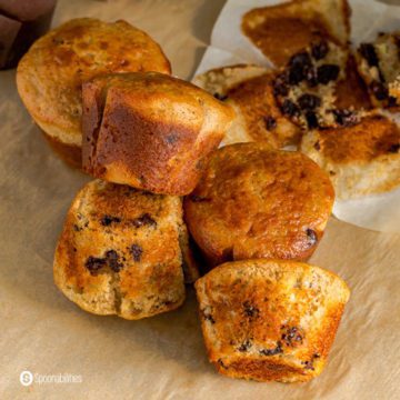 Six Sourdough muffins on a parchment paper and one of them is in the back of the photo. Recipe at Spoonabilities.com