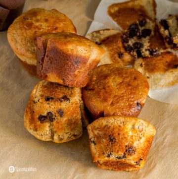 Six Sourdough muffins on a parchment paper and one of them is in the back of the photo. Recipe at Spoonabilities.com