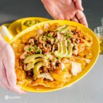 Two hands holding a yellow oval serving plate with loaded vegan nachos. Recipe at Spoonabilities.com