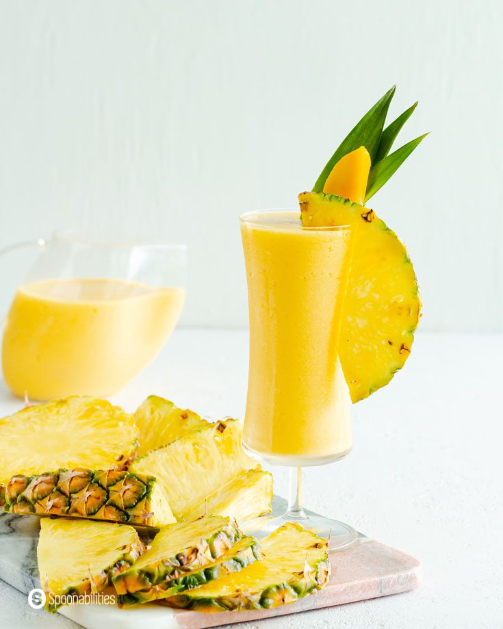 slices of pineapple next to a tall glass of mango pina colada