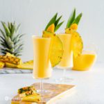 slices of pineapple next to a tall glass of mango pina colada