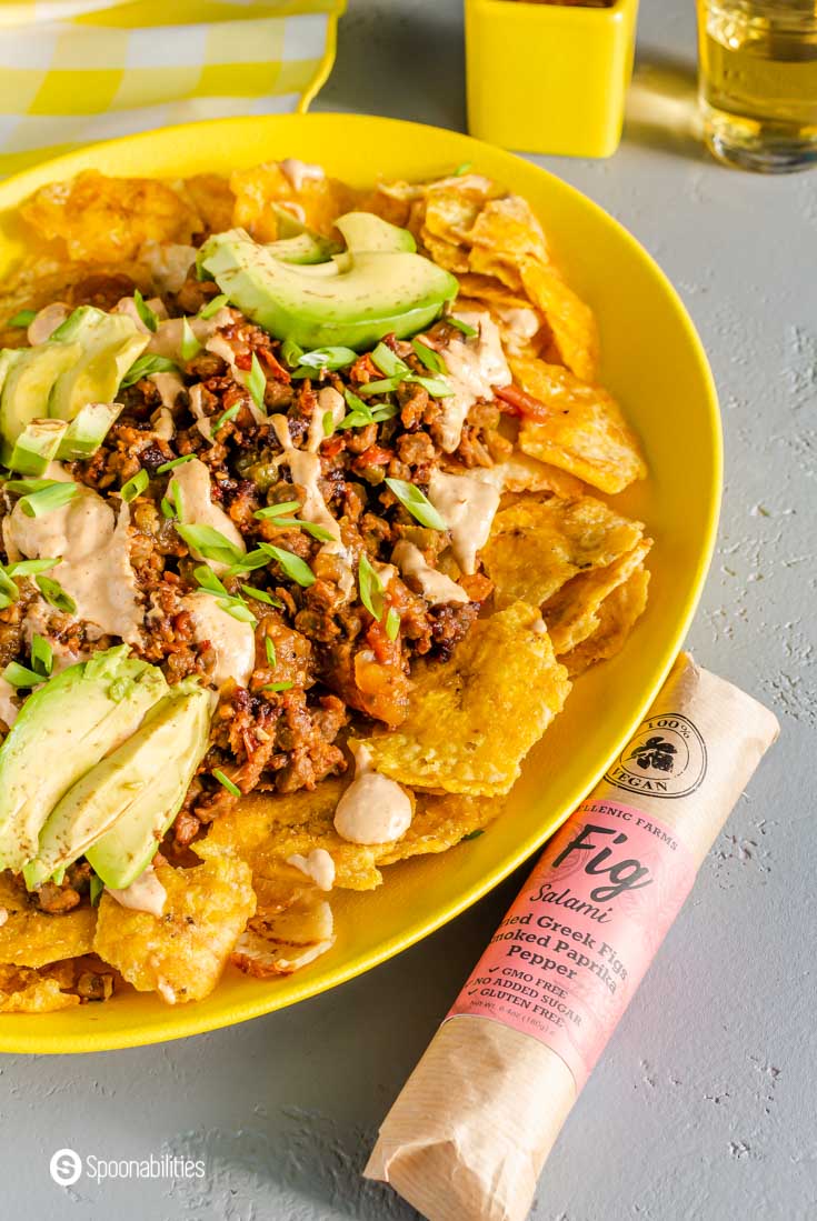 A Vegan Fig Salami with Paprika next to a yellow plate with nachos. 