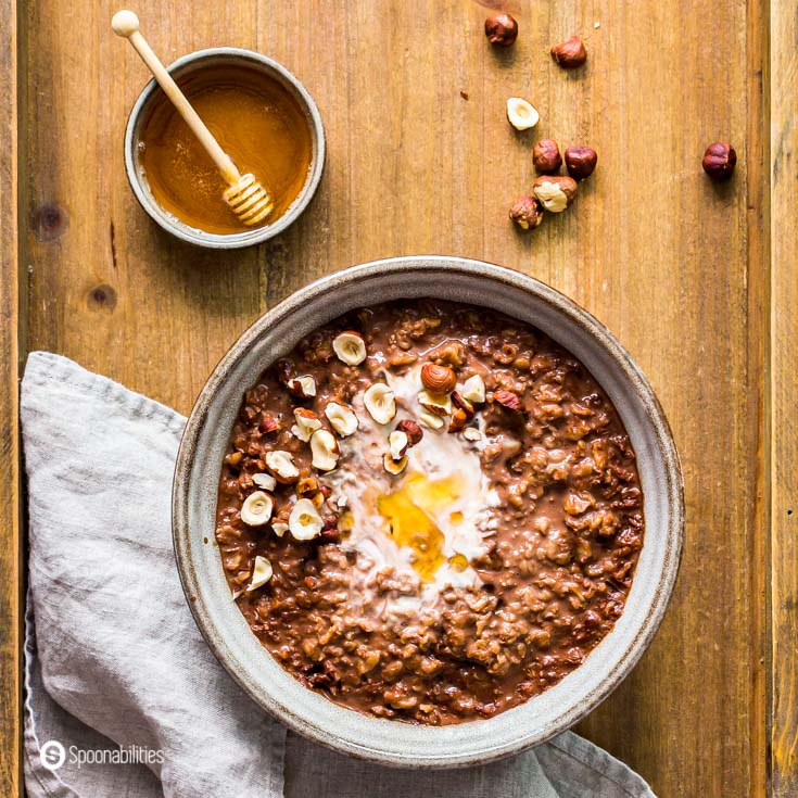 closeup of chocolate oatmeal in a white bowl next to dish of honey