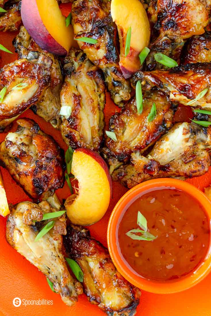 close up overhead photo of chicken wings, pepper peach sauce and sliced peaches