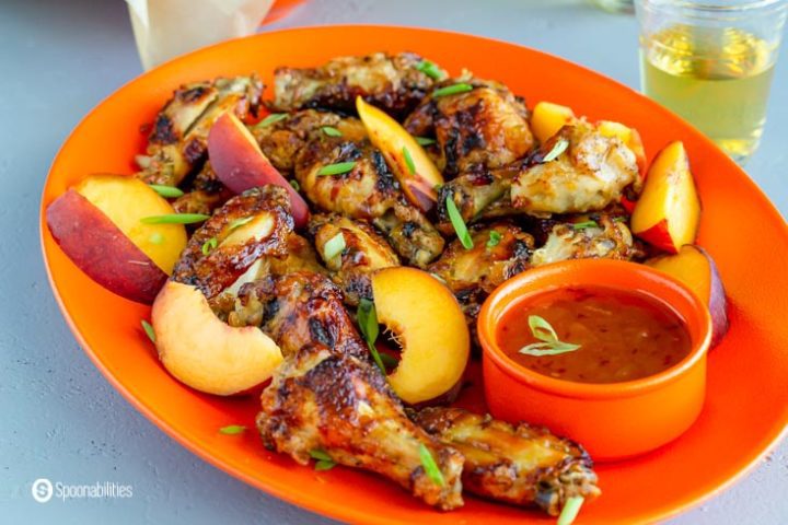 orange plate with air-fryer chicken wings, sauce and peaches on the side