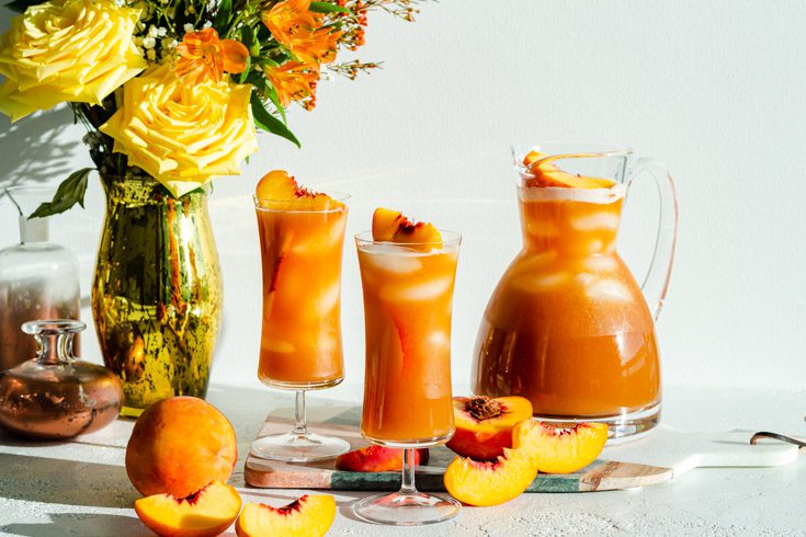 Large pitcher of peach iced tea next to 2 tall glasses of the same