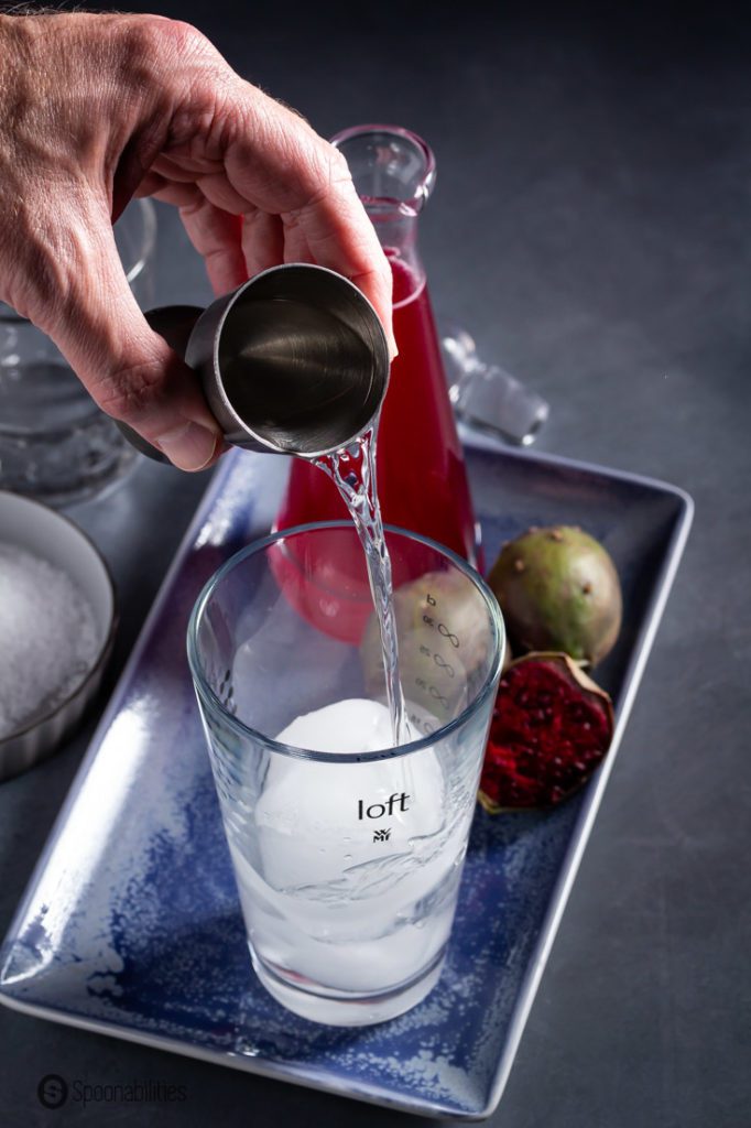 A hand pouring Tequila blanco to a glass mixing glass.