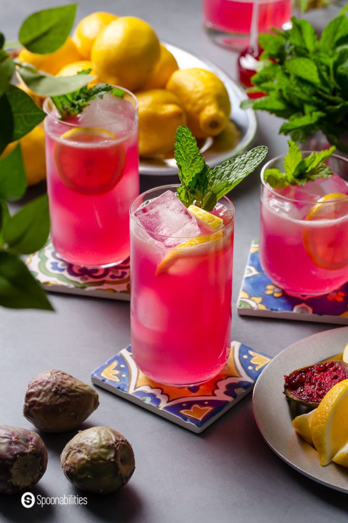 Two tall glasses and one rock glass with Prickly Pear Juice Lemonade, garnished with fresh mint.