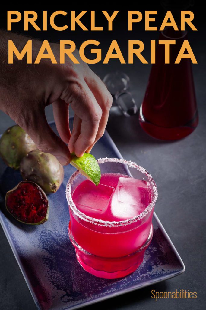 A rock glass with prickly pear margarita and a hand putting a lime on the glass. Recipe at Spoonabilities.com