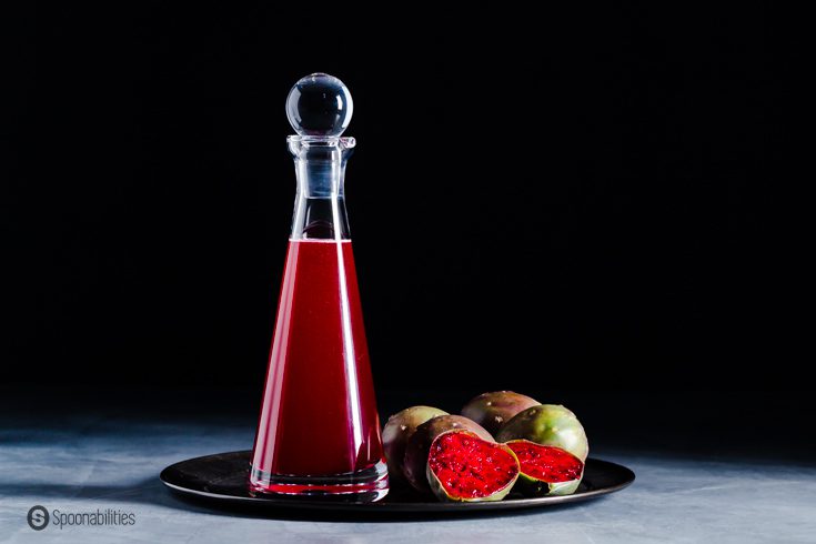 A glass bottle on top of a metal tray. The bottle has flavored simple syrup with prickly pear. Recipe at Spoonabilities.com