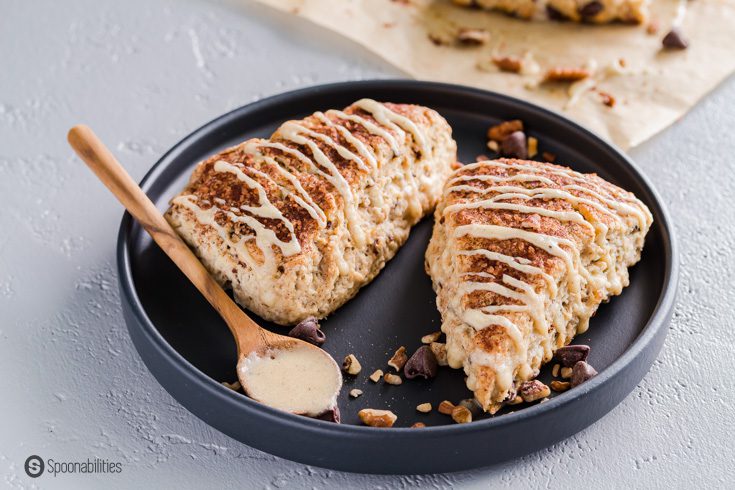 A black plate with two scones and a spoon with brown butter maple glaze. Recipe at Spoonabilities.com