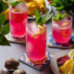 Three glasses on top of a coaster with Prickly Pear Juice Sparkling Lemonade and garnished with fresh mint and sliced lemon.