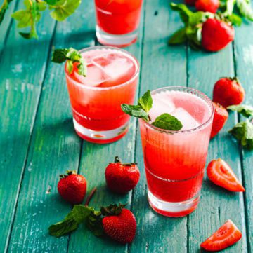Two clear glasses of strawberry mint iced tea next to whole strawberries