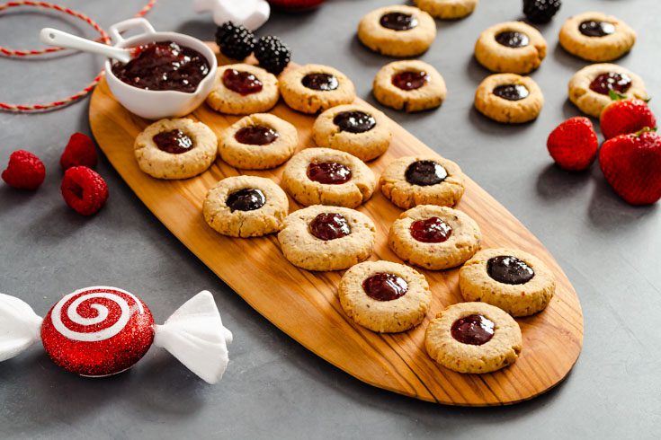 Wooden olive board with several almond cookies filled with a dollop of jam.