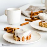 White plate with one Sourdough Cinnamon Rolls. In the background more cinnamon buns and cups with coffee.