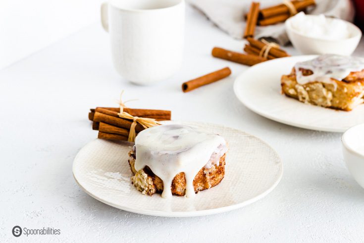 Two small round white plates with cinnamon roll and cream cheese icing.