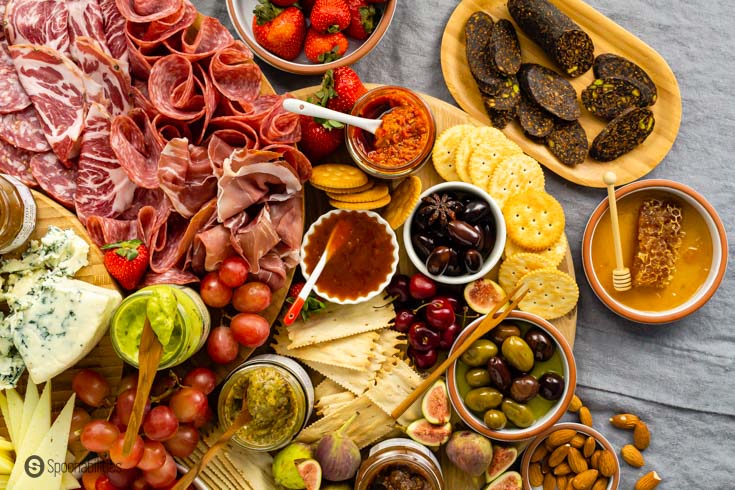 Charcuterie board with unique dip options like chutney, honey, pesto, and baba ganoush.