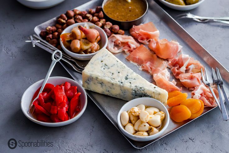 Charcuterie board with blue cheese, prosciutto, fruit, and nuts, along with serving utensils