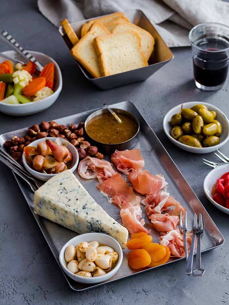 Metal tray with blue cheese, prosciutto, olives, toasts and other charcuterie items