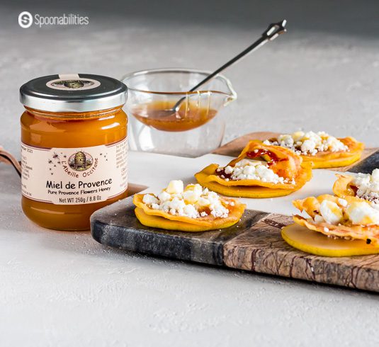 A jar of honey Miel de Provence and next to the jar is a marble board with Pear, prosciutto, goat cheese, and a drizzle of honey.
