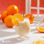 A beautiful glass with the Dominican drink Morir Sonando. The photo is bright in a white background with some oranges in the back as a decor.