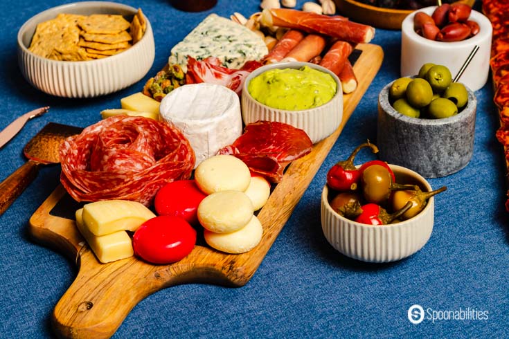 charcuterie board with selection of meats, cheeses, olives, peppers, crackers, and gourmet mustard