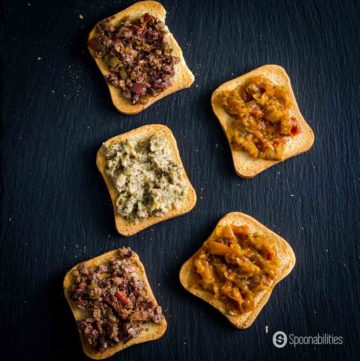 Five Crostini topped with olive tapenade, tapenade with dried tomato and basil, basil pesto, and fig Chutney.