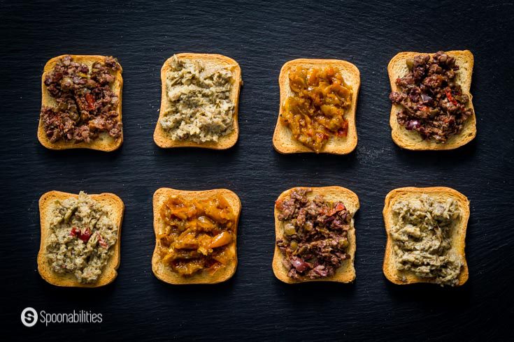 crostini with various toppings shown on a black slate charcuterie board