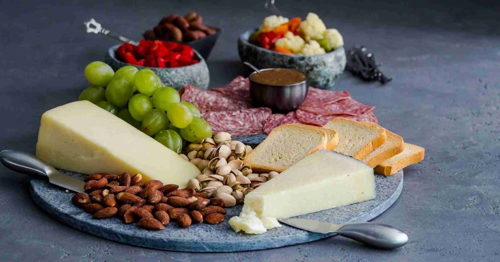 Charcuterie board featuring hard white cheese, nuts, grapes, salami, bread, and veggie bites