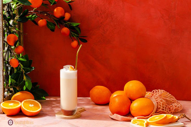 A set decorated simulating the gardens of Sevilla, Spain with orange branches and oranges on the floor. A drink in the center with an orange creamsicle alcoholic drink.