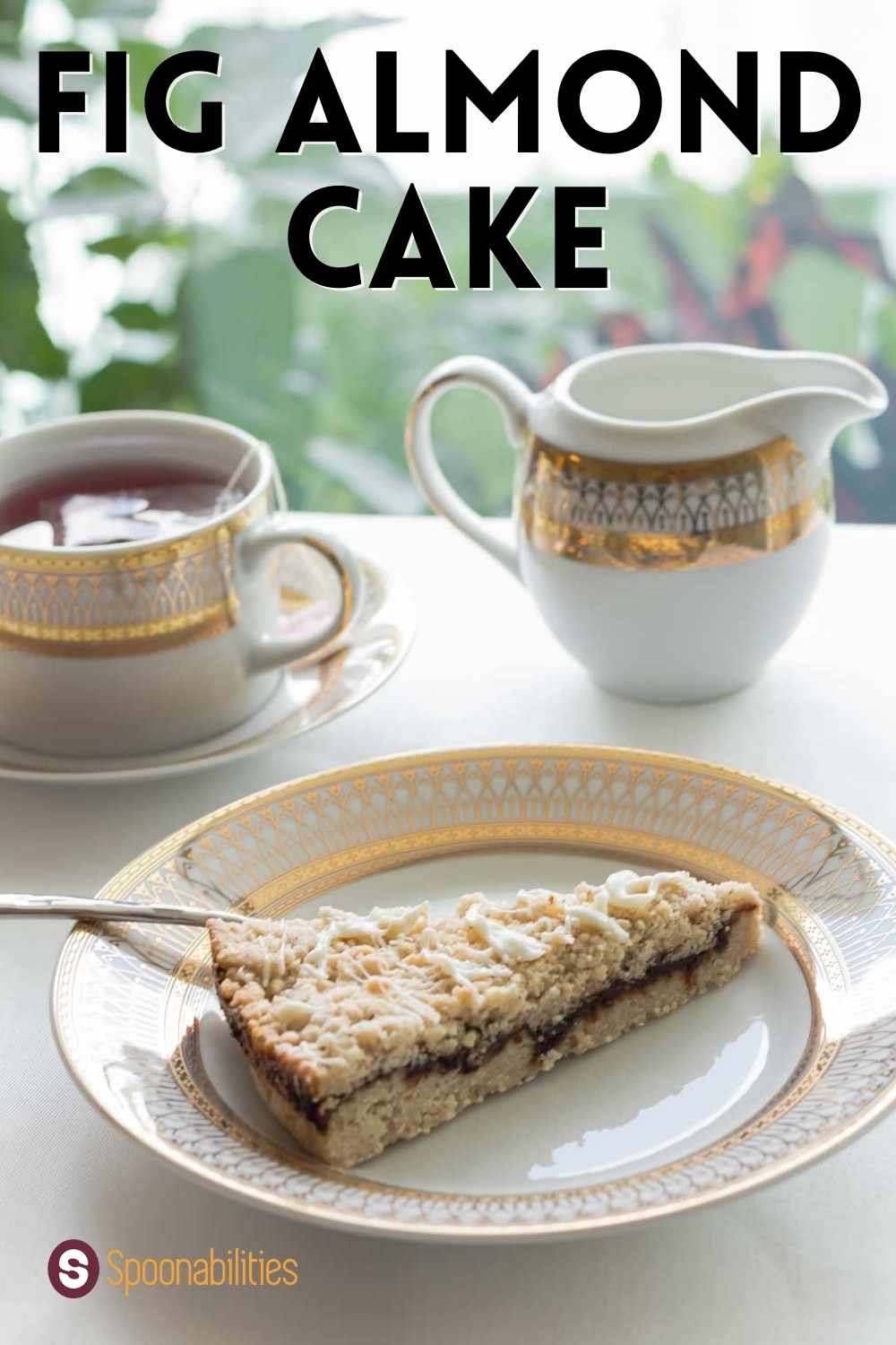 Slice of Fig Almond Cake on a gold-rimmed cake plate along with a cup of tea and pitcher of milk