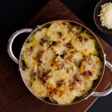 Pot of Leek and Potato Gratin on a wood board next to grated cheese