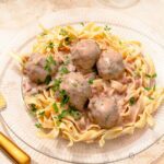 close up of 5 Swedish meatballs with lingonberry sauce on a glass plate with egg noodles.