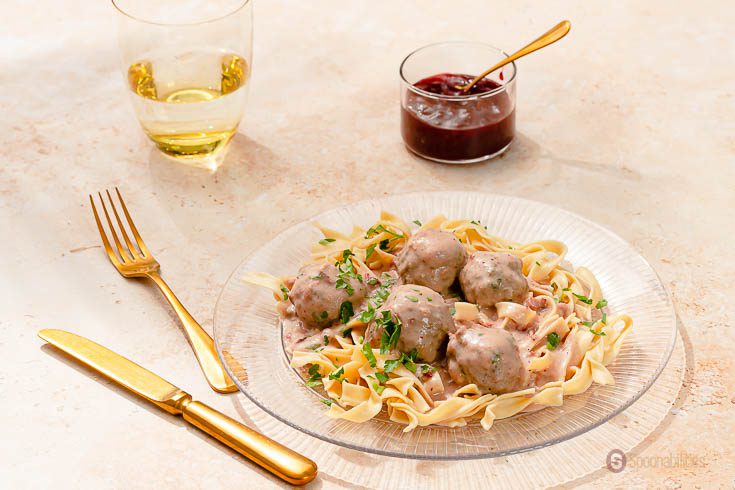 glass plate of Swedish Meatballs on egg noodles with Lingonberry Fruit Spread on the side